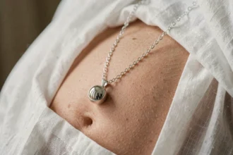 Bola de grossesse en argent posé sur un ventre rond recouvert de lin blanc