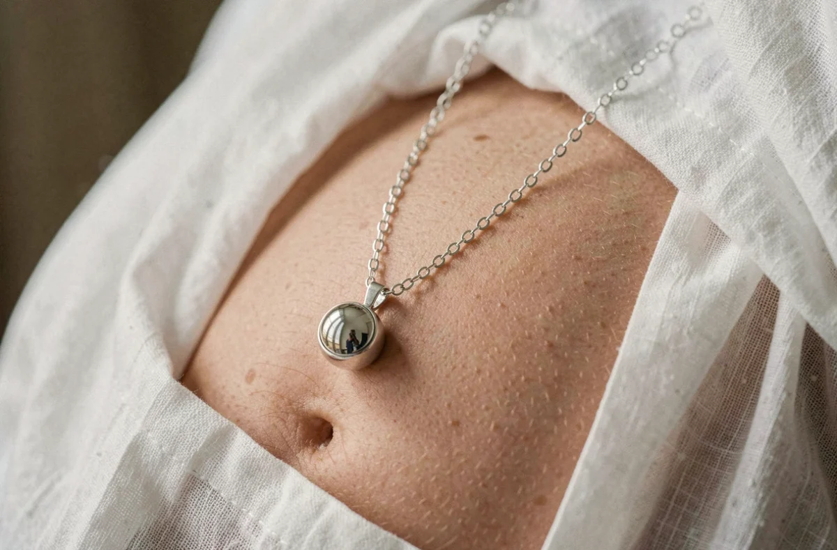 Bola de grossesse en argent posé sur un ventre rond recouvert de lin blanc