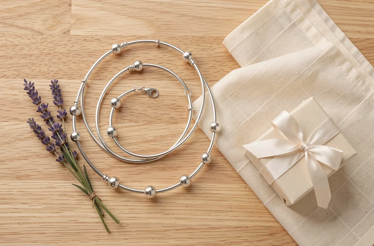 Bola de grossesse en argent en flat lay avec lavande séchée et boîte cadeau sur bois clair